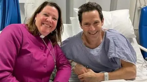 Andrew Rawding Andrew Rawding sitting up in his hospital bed, while the Bishop of Southampton sits beside him in a cassock