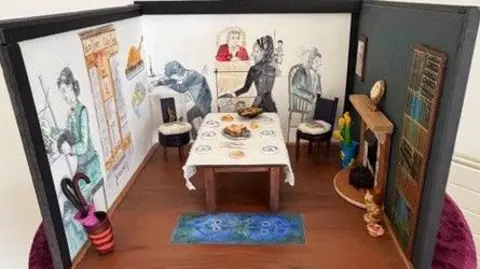Amanda Pearce A model of the scene of the murder. It is a shoebox-sized display with drawings of people around the walls and a small dining table in the middle of the room.