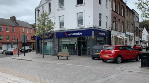 A Nationwide branch with cars parked around it and a bench in front