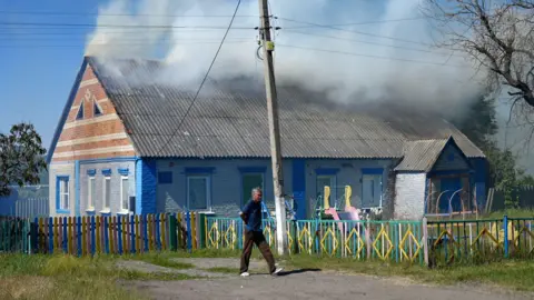 Man walks in front of a kindergarten building with smoke rising from its roof