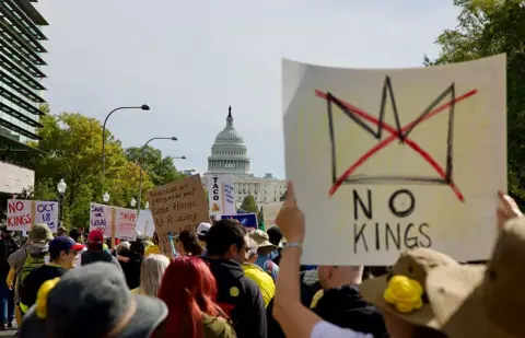 Getty Images protestētāji dodas gājienā pie Kapitolija ēkas Vašingtonā, DC. Viens cilvēks nēsā zīmi, kas lasa "Nav karaļu".