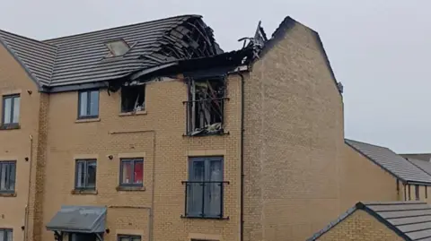 Shane Proctor A building with its roof collapsed and burnt out. The bricks are yellow and it is an overcast day.