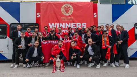 Jack Valpy/BBC The team standing with the cup in front of the bus.