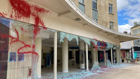 Red spray paint on Barclays' windows with smashed glass on the ground 