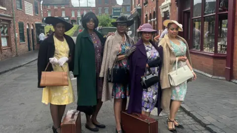 A group dressed in vintage fashion stands along a cobbled stree