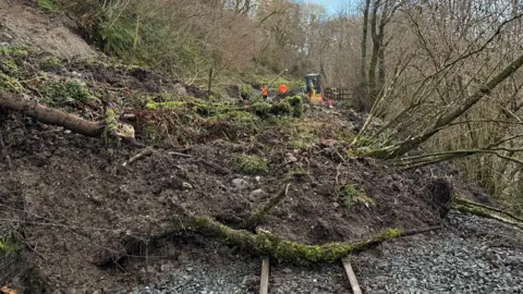 Ffestiniog Railway Company Workers in hi-viz jackets survey debris blocking the rail line