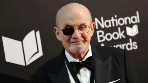 Getti, Sir Salman Rushdie, a photographer wearing an evening and a black tie. He wears glasses, with a dark one side after blinded.