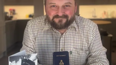 EMMAUS DOVER Ross McEwen poses with the bible and a picture of a Shorts Sterling. He has a beard and wears a brown and white checked shirt.