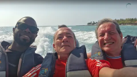 L-R Yostin Mosquera, Albert Alfonso and Paul Longworth. They are shown smiling in a selfie, all wearing life jackets as they sit at the back of a speedboat.