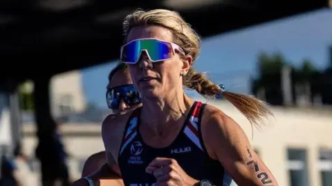 Duathlon World Championships Zoe Tucker competing with a blue GBR running vest, the number 1720 on her arm, and a stadium of spectators behind her.