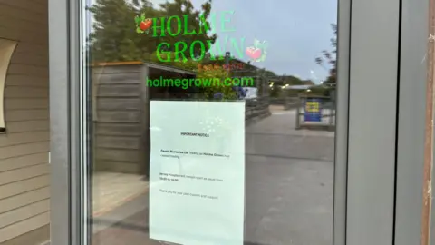BBC The front window of the building showing a glass door. It has the green logo for Holme Grown and a signing saying the company had ceased trading.