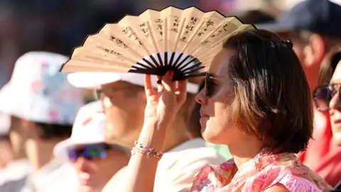A woman fans herself in the heat at Wimbledon in London, England on 11 July 2025.