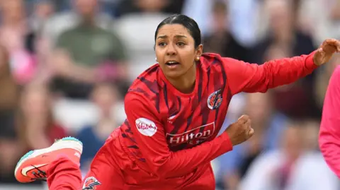 Alana King, wearing a red Lancashire shirt, bowls a ball