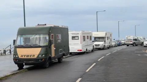 A row of motorhomes parked on a seafront on a grey day. 