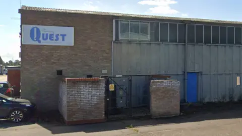 The exterior of a small industrial unit made of brick and metal panelling. It has a sign that says "The Engineering QUEST" on it