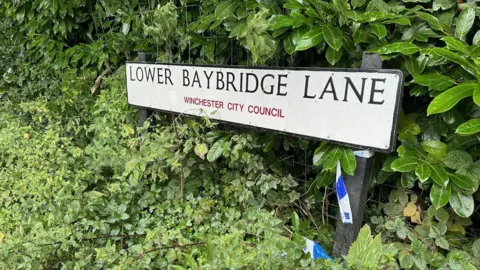 BBC Police tape can be seen around the road sign for Lower Baybridge Lane