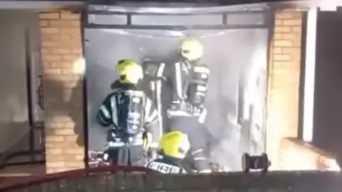 Three firefighters wearing yellow helmets and black and white gear in a smoky building.