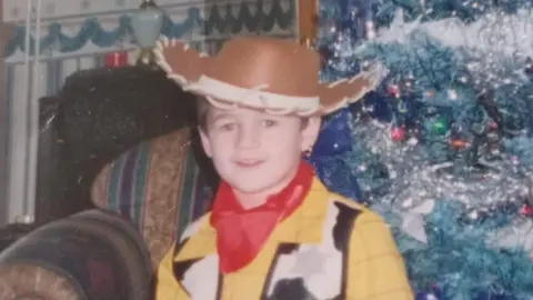 Family handout A photograph of Kaine Fletcher as a child, wearing a Woody costume, from Toy's Story', standing in front of a Christmas tree