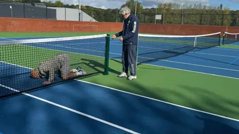Simon Thake A man kneels down kissing a green and blue tennis court