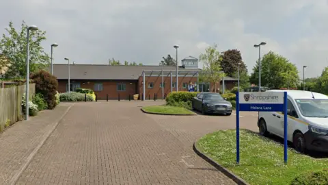 A Google street view image of the entrance of the centre. A Shropshire Council sign can be seen on the right which reads "Helena Lane". There are two vehicles parked in a car park and a community centre building in the background.