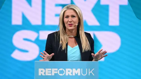 AFP Laura Anne Jones stood in front of a podium that reads Reform UK in capital letters.