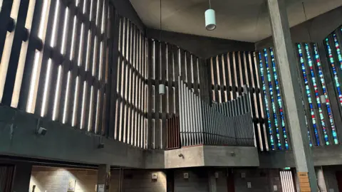 Church of the Good Shepherd Inside the church, showing a high ceiling with bar-like windows holding stained glass and a large church organ