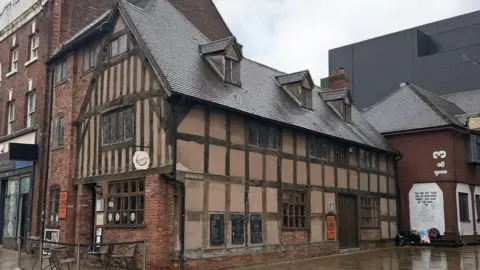 Bond Wolfe The side view of a 1600s style three story red brick building with timber panelling 