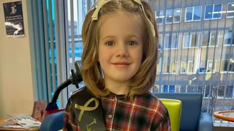 A young girl with light hair in bunches and a tartan top