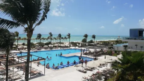 Colin Nulty Pool side view of the Riu Palace Costa Mujeres in Cancun showing guests sunbathing and swimming and the beach in the background on a sunny day.
