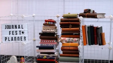 Planner UK White crates are stacked on top of one another. A pile of brown and tan coloured leather books are sitting inside the crates.