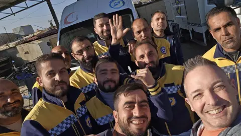 Fergus Beeley A group of paramedics in yellow uniform are taking a selfie together and all are smiling.