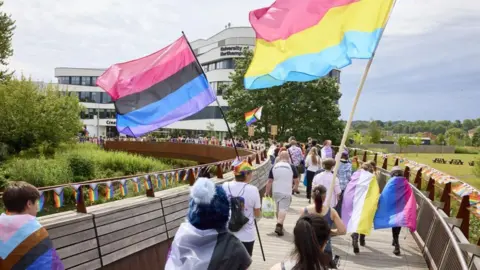 People waving Pride flags, with their backs turned, walking away from the camera on the University of Northampton campus