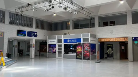 Harriet Heywood/BBC A mostly white space in the cresset shows one of the other venues inside, The Fayre Spot - a pub. The floor is white and the walls are also a white brick. There are adverts for different shows around the room.
