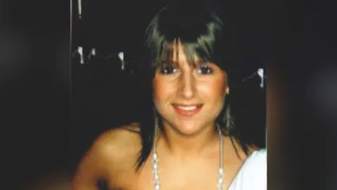 Family photo Jenna Watkins is a white woman in her early 20s in a head and shoulders photo. She has dyed black hair which is shoulder length with a fringe. She is wearing an off the shoulder white top and a long silver necklace with large beads starting at her collarbone. She is wearing make up and looks like she is on a night out. She is smiling straight at the camera. The background is black.