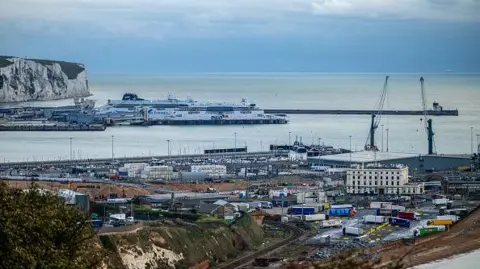Getty Images A wide view of Dover shows ferries docked at a busy port with cranes, lorries and buildings in the foreground, and white cliffs visible along the coastline beyond.