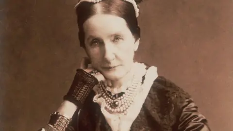 Getty Images Angela Burdett-Coutts, a middle-aged woman wearing a dark dress and pearls, poses leaning on her right hand in a Victorian portrait photograph.