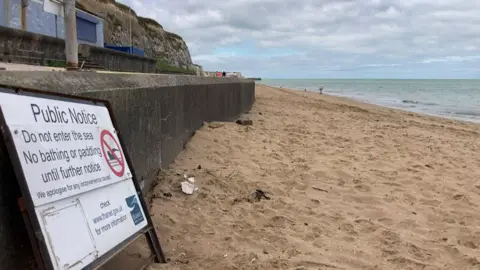 A sign warning not to enter the sea propped against a wall on a sandy beach
