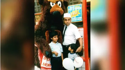 Morley's A man, two children, and a person in a bear costume stand outside a Morley’s Fried Chicken shop.