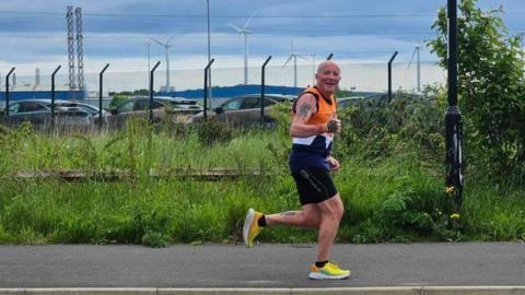 Paul running on a pavement with wind turbines behind