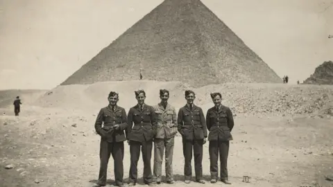 IBCC A group of five uniformed airmen, all wearing side caps, lined up in front of Great Pyramid of Giza (Pyramid of Khufu) at the Giza Necropolis, Egypt.