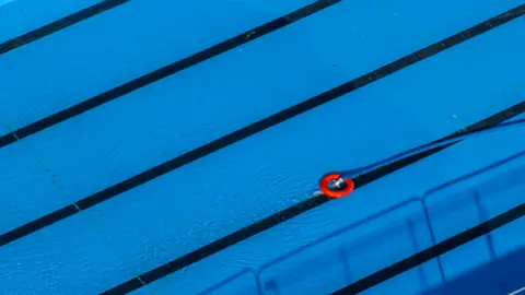 A blue hosepipe with bright red lifering on the end, floating in a vivid blue laned swimming pool