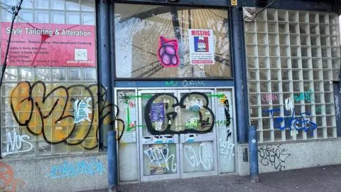 A wall with grey brickwork and small glass squares covered with graffiti