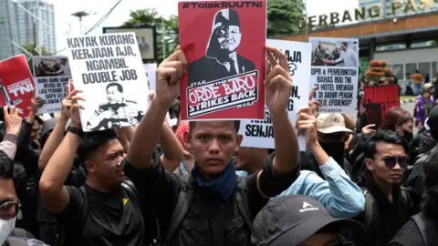 EPA Activists hold placards during a protest against the revision of the country's military law in front of the Parliament building in Jakarta, Indonesia, 20 March 2025. At the centre is a man in a black long-sleeved top holdoing a piece of paper with President Prabowo Subianto's caricature on it. 