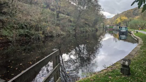 Alex Moss/BBC A picture of a river surrounded by hills and trees with several barges moored on the riverside. 