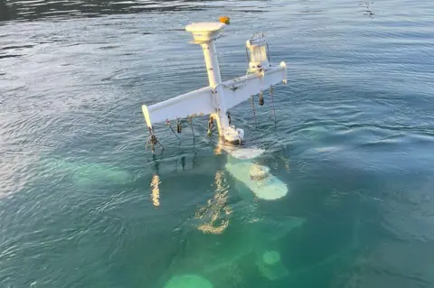 RNLI Oban Lifeboat Station The white communications mast on the fishing boat above the surface of a calm sea. The top of the boat's wheelhouse is just visible under the water.