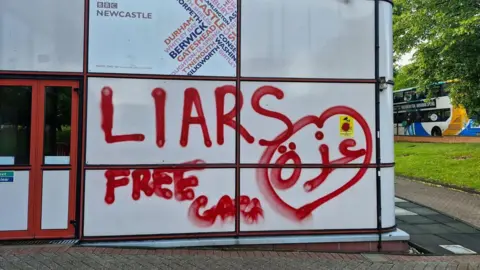 White panelled exterior wall of BBC Broadcasting Centre. Underneath the BBC Newcastle sign are the words "Liars" and "Free Gaza" sprayed with red paint, along with the Arabic for Gaza and a squashed heart shape.