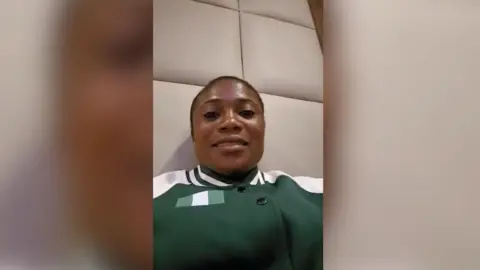 Portrait image of Goodness Chiemerie Nwachukwu (taken on a phone). She is black and has dark hair tied back. She's wearing a green and white sports jacket and looking straight at the camera