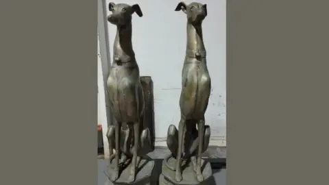 Dorset Police Two dog statues depicting slim large dogs sitting upright on plinths - they have identical collars.