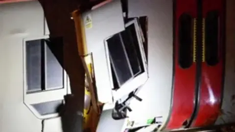 Dan Jones Close-up image of train carriage in the dark with smashed window and damage to side