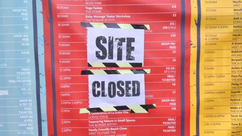 A red, blue and yellow poster showing an itinerary of events with paper taped over it saying SITE CLOSED